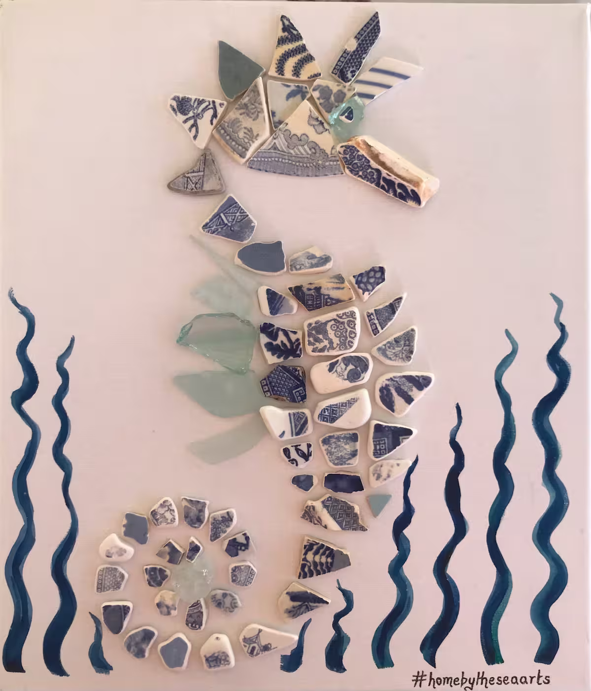 Seahorse artwork crafted from blue and white sea pottery with sea foam sea glass fins and eye, set against painted seaweed on a 35x30cm canvas.